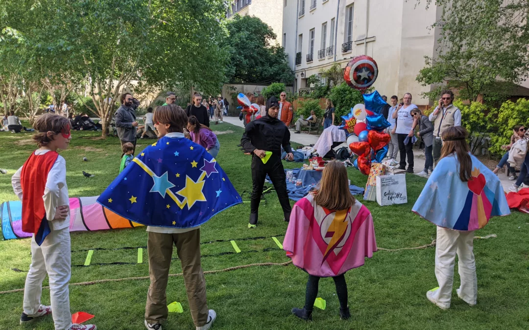 Animateur déguisé et enfant en costume fêtant un anniversaire en plein air, entourés de parents souriants qui les regardent.